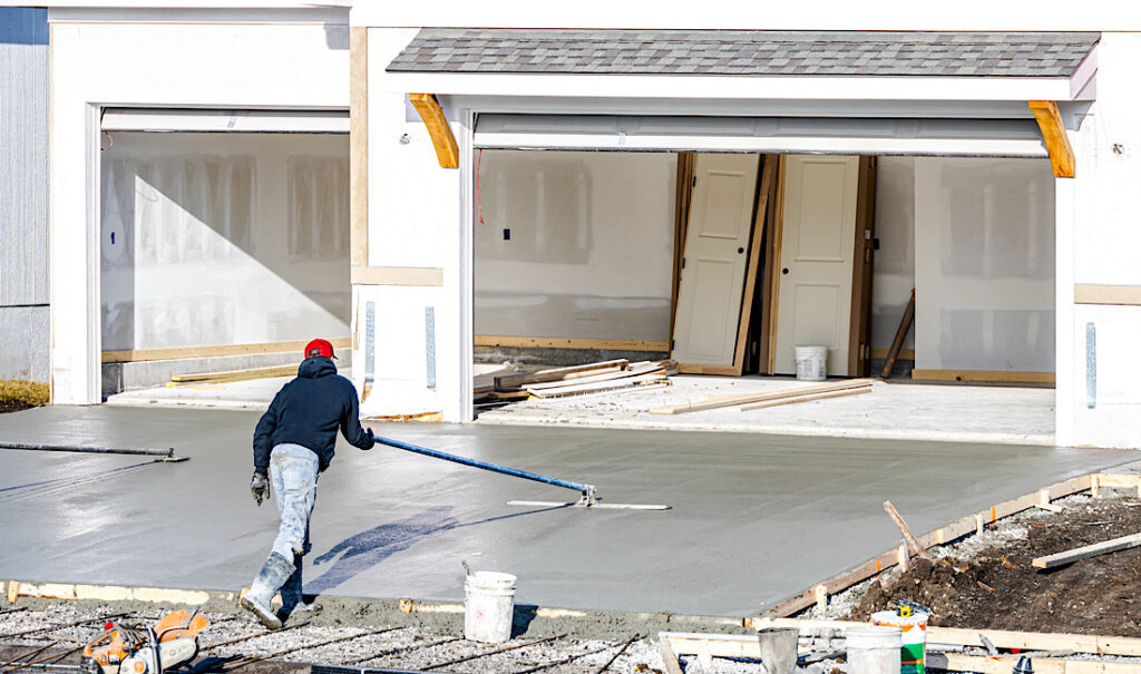 Man working on smoothing concrete driveway for the new home build at construction site in Denver, CO.